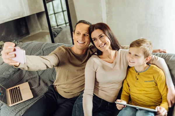 Веселая семья делает селфи на диване — стоковое фото