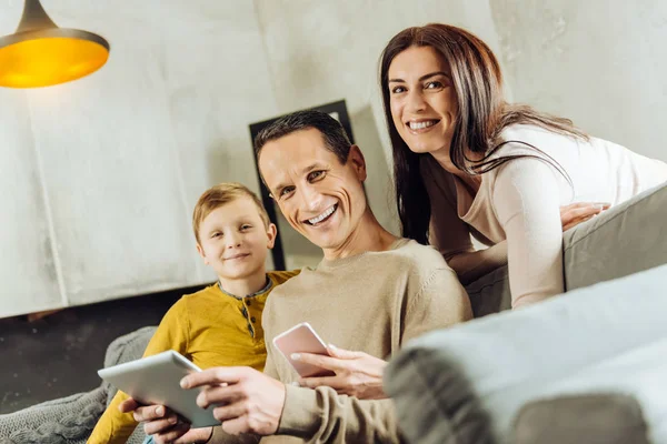 Молодая семья держит гаджеты и улыбается — стоковое фото