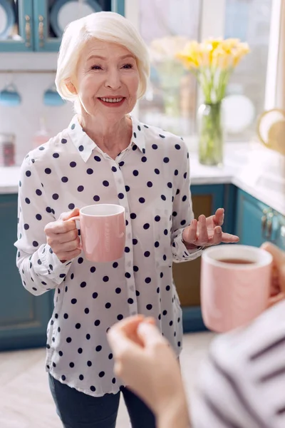 Mujer mayor bebiendo café en la cocina y hablando —  Fotos de Stock