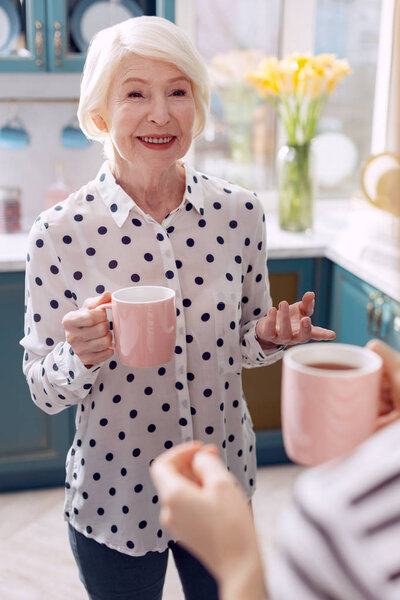 Elderly woman drinking coffee in kitchen and talking