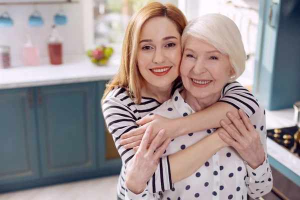 Femme heureuse étreignant sa mère aînée dans la cuisine — Photo