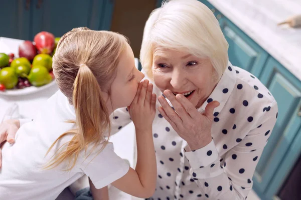 Fröhliches Mädchen und ihre Großmutter teilen Geheimnisse — Stockfoto
