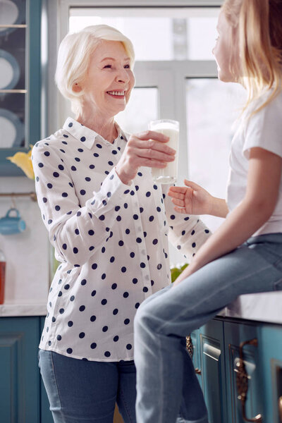 Pleasant woman offering her granddaughter to drink milk