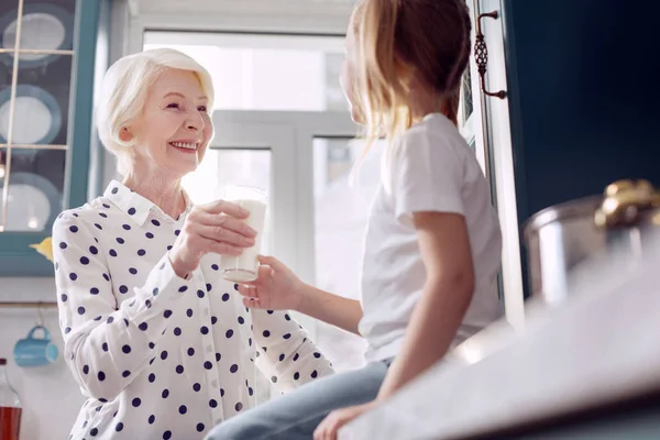 Cuidar a la mujer mayor dándole un vaso de leche a su nieta —  Fotos de Stock