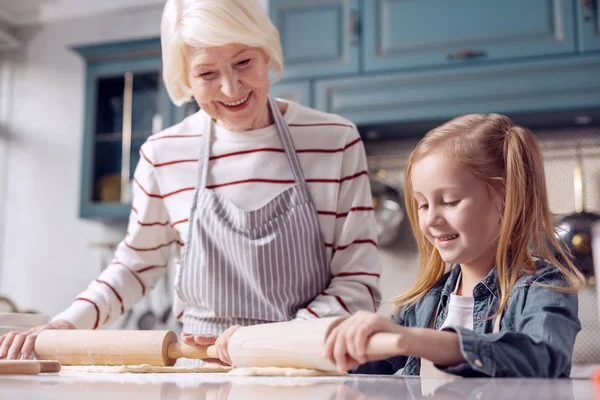 Little girl rolling out dough with her grandmother