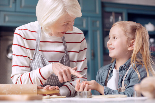 Pleasant woman pointing at cookie in her granddaughters hands