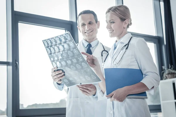 Médicos calificados atentos que pasan por alto la exploración de rayos X y sonriendo . — Foto de Stock