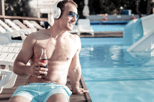Beaming millennial guy listening to music and sunbathing outdoors