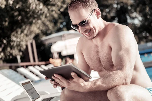 Extremely happy millennial guy looking at tablet computer and smiling — Stock Photo, Image