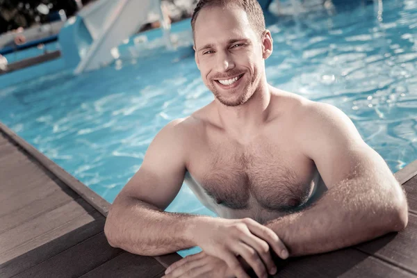 Bem construído cara milenar sorrindo enquanto nadava na piscina — Fotografia de Stock