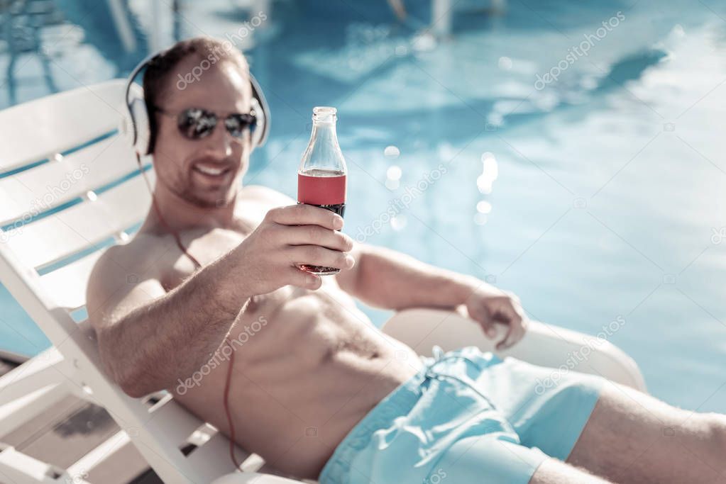 Joyful gentleman drinking sparkling water and sunbathing