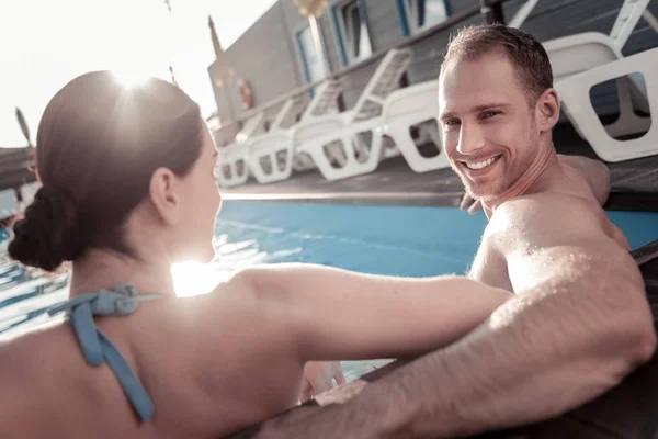 Radiant millennial guy smiling into camera while sitting in pool — Stock Photo, Image