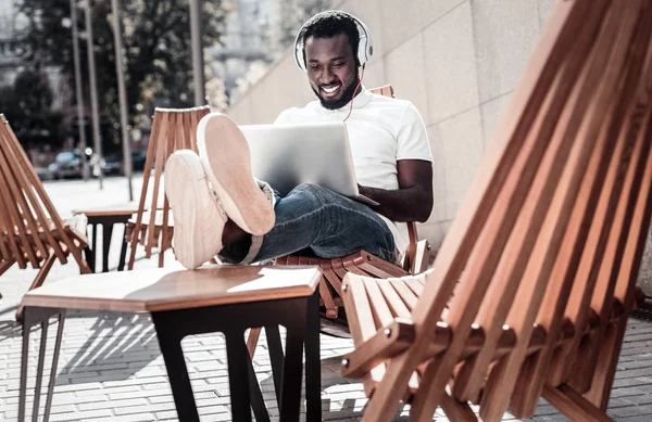 Χαρούμενη αφρικανική αμερικανική τζέντλεμαν, ακούγοντας μουσική, ενώ χρησιμοποιούν φορητό υπολογιστή — Φωτογραφία Αρχείου