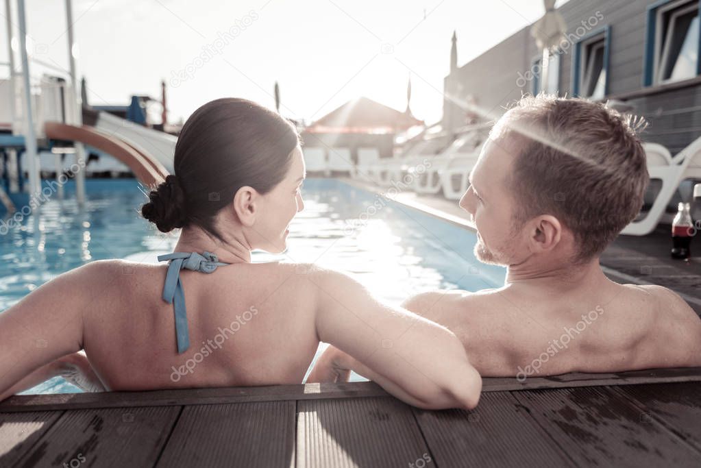 Relaxed couple sitting in swimming pool and chatting