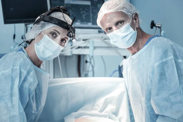 Gekwalificeerde verantwoordelijk dokters op zoek rechte en staande in de buurt van die van tabel. — Stockfoto