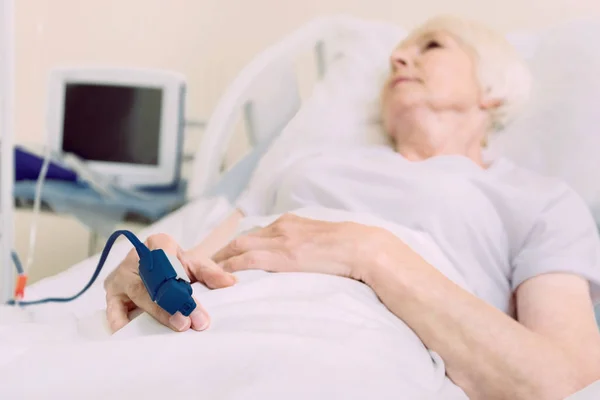 Chudák starší dáma leží v nemocniční posteli s Pulsní oxymetr — Stock fotografie