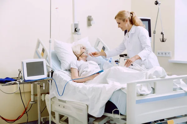 Γυναίκα γιατρός προσαρμογή αναπνευστική υποστήριξη ενώ στέκεται δίπλα στον ασθενή — Φωτογραφία Αρχείου