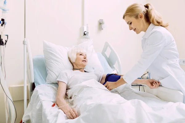 Médico sonriente revisando la presión arterial en el hospital —  Fotos de Stock