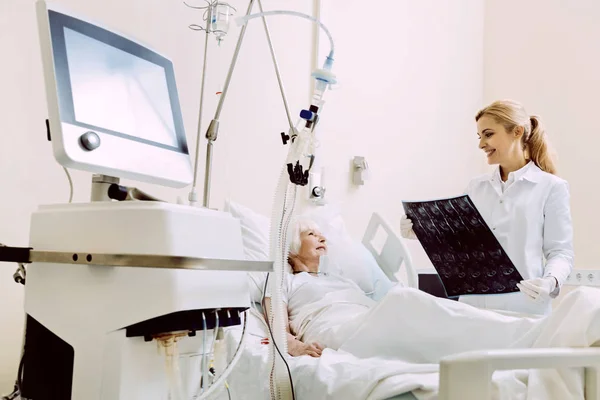 Médico sorridente olhando para exames de ressonância magnética de paciente sênior — Fotografia de Stock