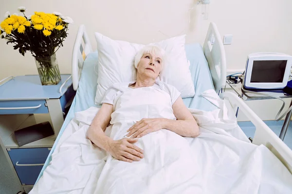 Zasněný starší žena v nemocniční posteli přemýšlet o něčem — Stock fotografie