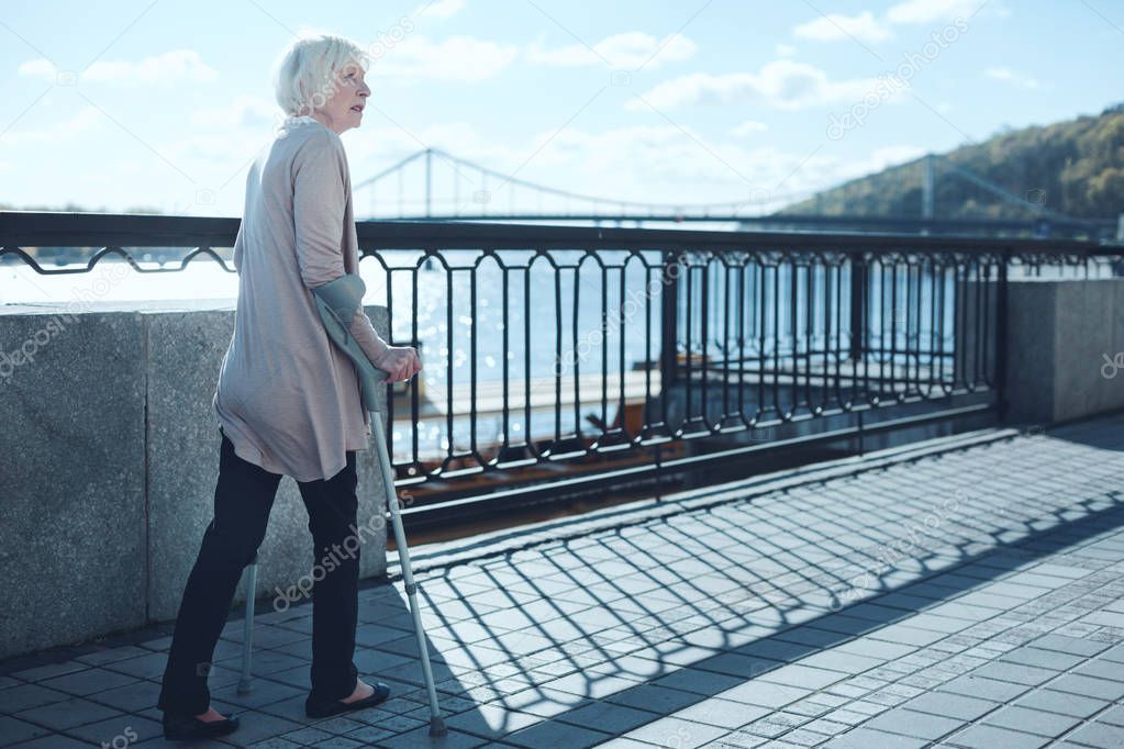 Worried senior woman staring somewhere while walking with crutches