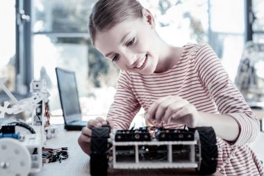 Beautiful girl smiling while constructing robotic vehicle clipart