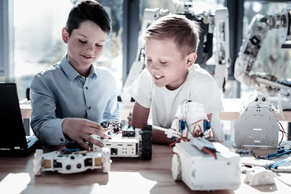 Relaxed kids constructing robotic machines with smiles on their faces — Stock Photo, Image