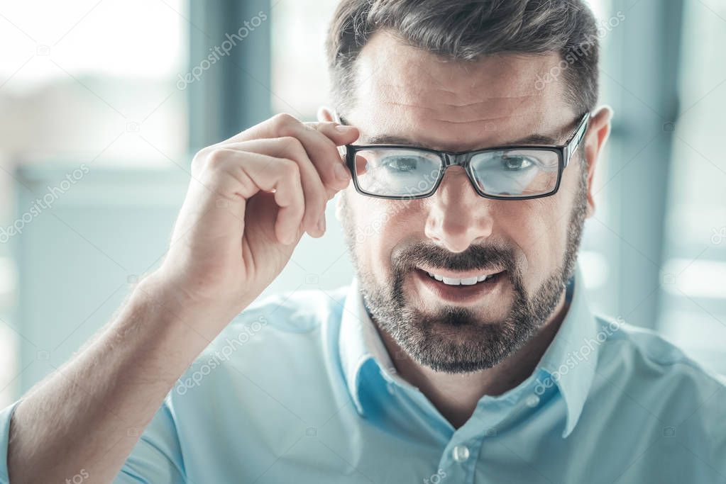 Delighted male person touching his glasses