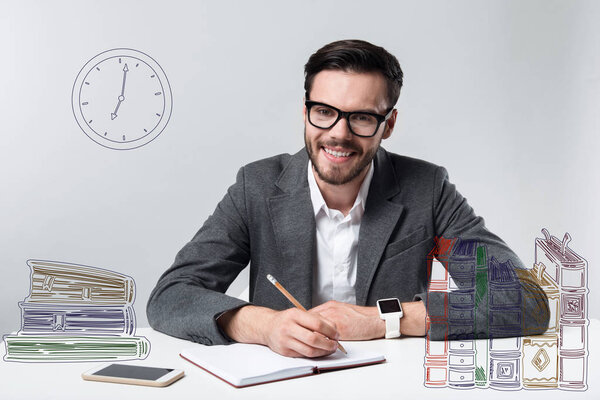 Working day. Positive experienced smiling man feeling glad while sitting in a comfortable office and making notes in his personal notebook