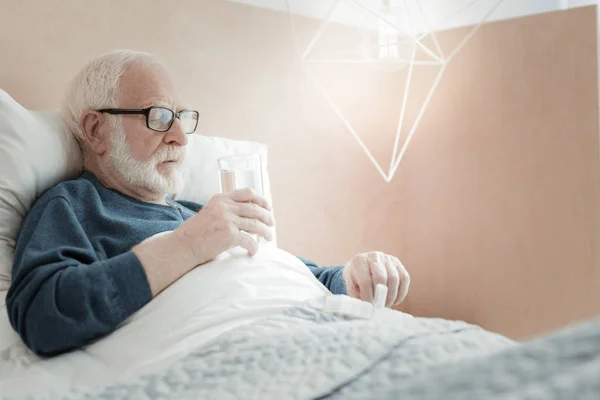 Koncentrované nemocný muž brát prášky a drží sklenici. — Stock fotografie