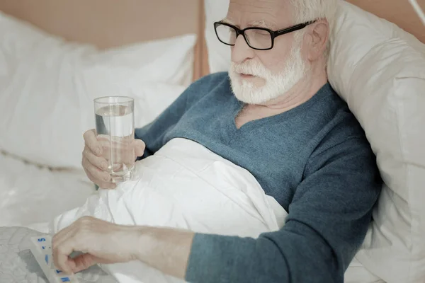 Hombre serio infeliz acostado y sosteniendo un vaso de agua . — Foto de Stock