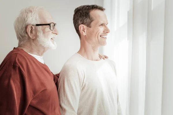 Satisfecho hombres agradables de pie y mirando por la ventana . — Foto de Stock