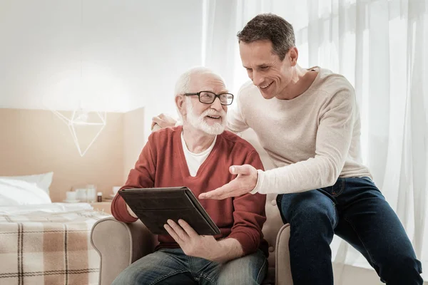 Divertidos hombres agradables sentado y con vistas a la tableta . — Foto de Stock