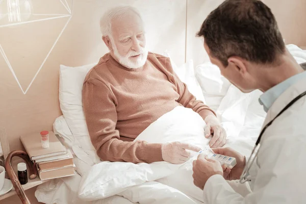 Tired senior man sitting and looking at pills. — Stock Photo, Image