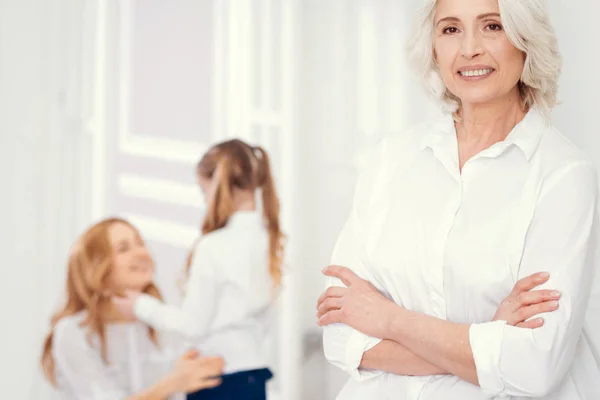 Beaming senior woman smiling into camera with family embracing behind — Stock Photo, Image