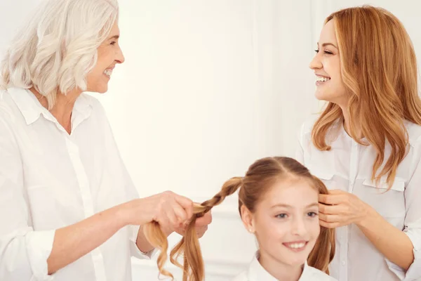 Radiant women smiling while making ponytails for little girl — Stock Photo, Image