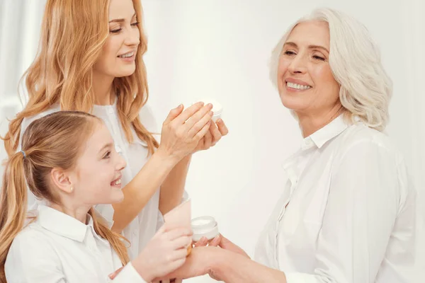Tender grandchild and mom applying cream on face of grandmother — Stock Photo, Image