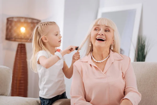 Positive blonde girl brushing her grandmothers hair — Stock Photo, Image