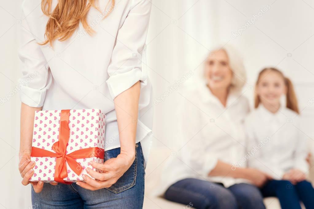 Close up of mature lady holding gift box behind back