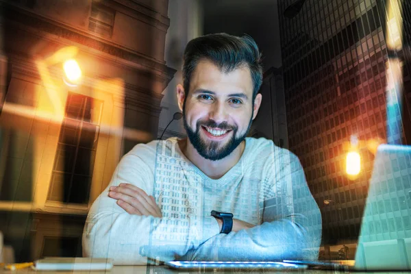 Handsome young man sitting with his laptop and looking glad — Stock Photo, Image