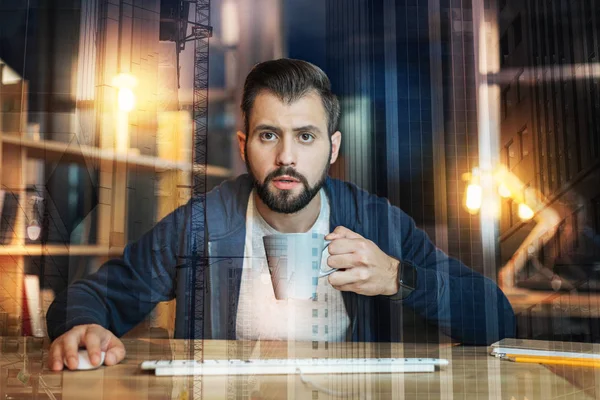 Hombre concentrado sosteniendo una taza y mirando a su monitor — Foto de Stock
