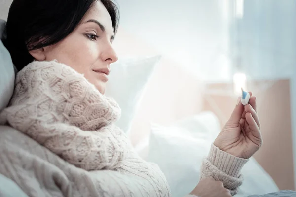Concentrated pleasant woman lying and holding a thermometer. — Stock Photo, Image