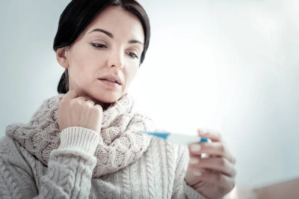 Sjuk ledsen kvinna holding och med utsikt över termometer. — Stockfoto