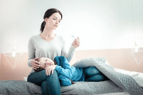 Κατεχόμενα φροντίδα γυναίκα που κρατά το θερμόμετρο αγγίζει στην κόρη της. — Φωτογραφία Αρχείου