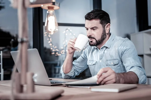 Hombre responsable concentrado bebiendo té y mirando la pantalla de los ordenadores portátiles . — Foto de Stock