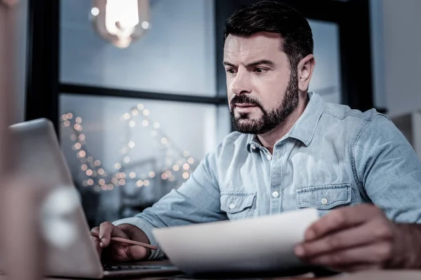 Upptagen stilig arbetstagare hålla dokumentet och använder sin laptop. — Stockfoto