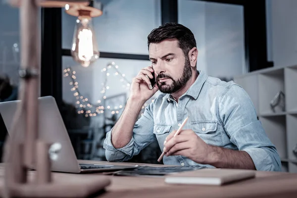 Occupied reliable employee having phone conversation and using his laptop.