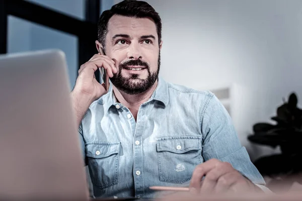 Hombre guapo satisfecho mirando a un lado y sosteniendo el teléfono celular cerca de su oreja . — Foto de Stock