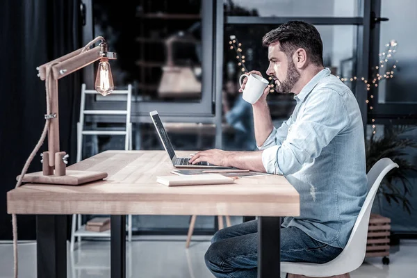 Sério homem ocupado usando o laptop e beber chá . — Fotografia de Stock