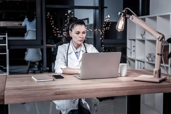 Συγκεντρώνεται το χαριτωμένο γιατρού κάθεται και εργάζεται με το φορητό υπολογιστή. — Φωτογραφία Αρχείου